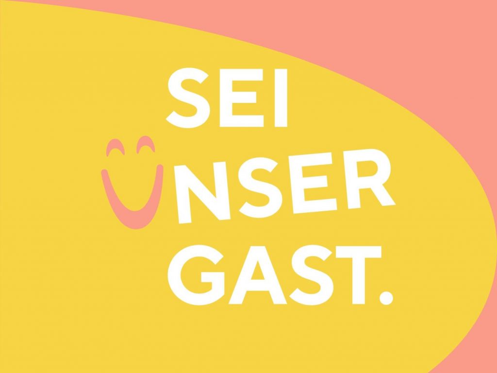 Auf einem gelben Hintergrund steht "SEI UNSER GAST" in Großbuchstaben.
